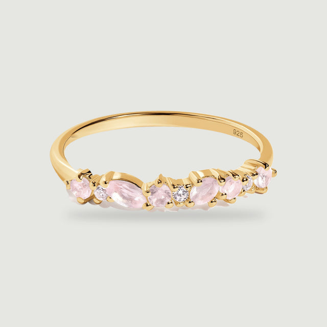 A yellow gold ring with pale pink rose quartz and small clear stones rests on a light gray surface.