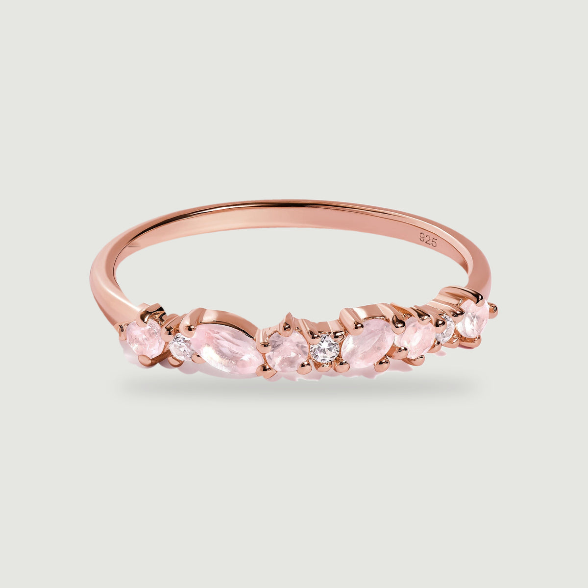 A rose gold ring curves around a row of pale pink gemstones and tiny clear stones on light gray.