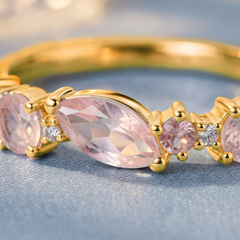 A close view shows a marquise pink gemstone beside round pink and clear stones in yellow gold prongs.