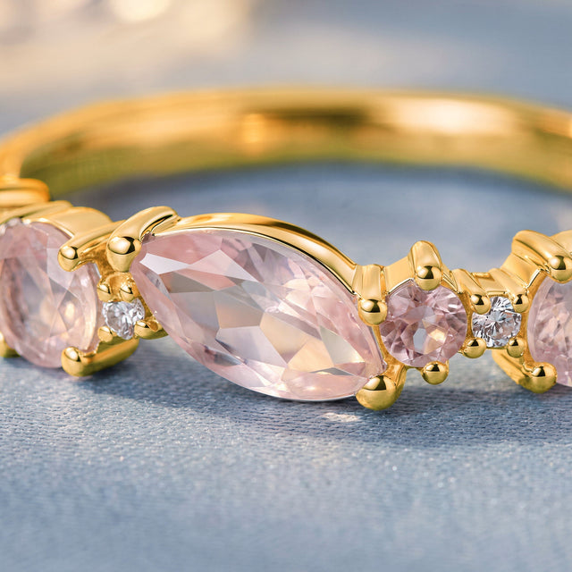 A close view shows a marquise pink gemstone beside round pink and clear stones in yellow gold prongs.