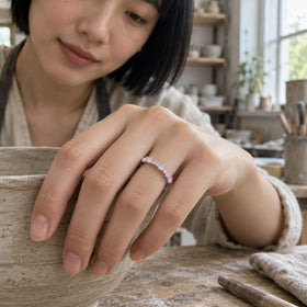 A silver ring with small pink stones sits on a woman's finger as her hand rests on a ceramic bowl in a pottery studio.