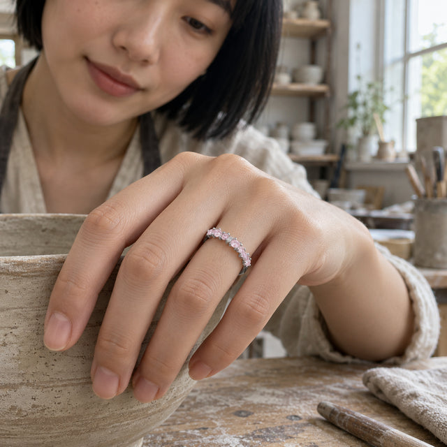 A silver ring with small pink stones sits on a woman's finger as her hand rests on a ceramic bowl in a pottery studio.
