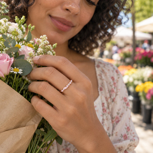 A curly-haired woman holds a flower bouquet with the pink stone rose gold ring visible on her hand.