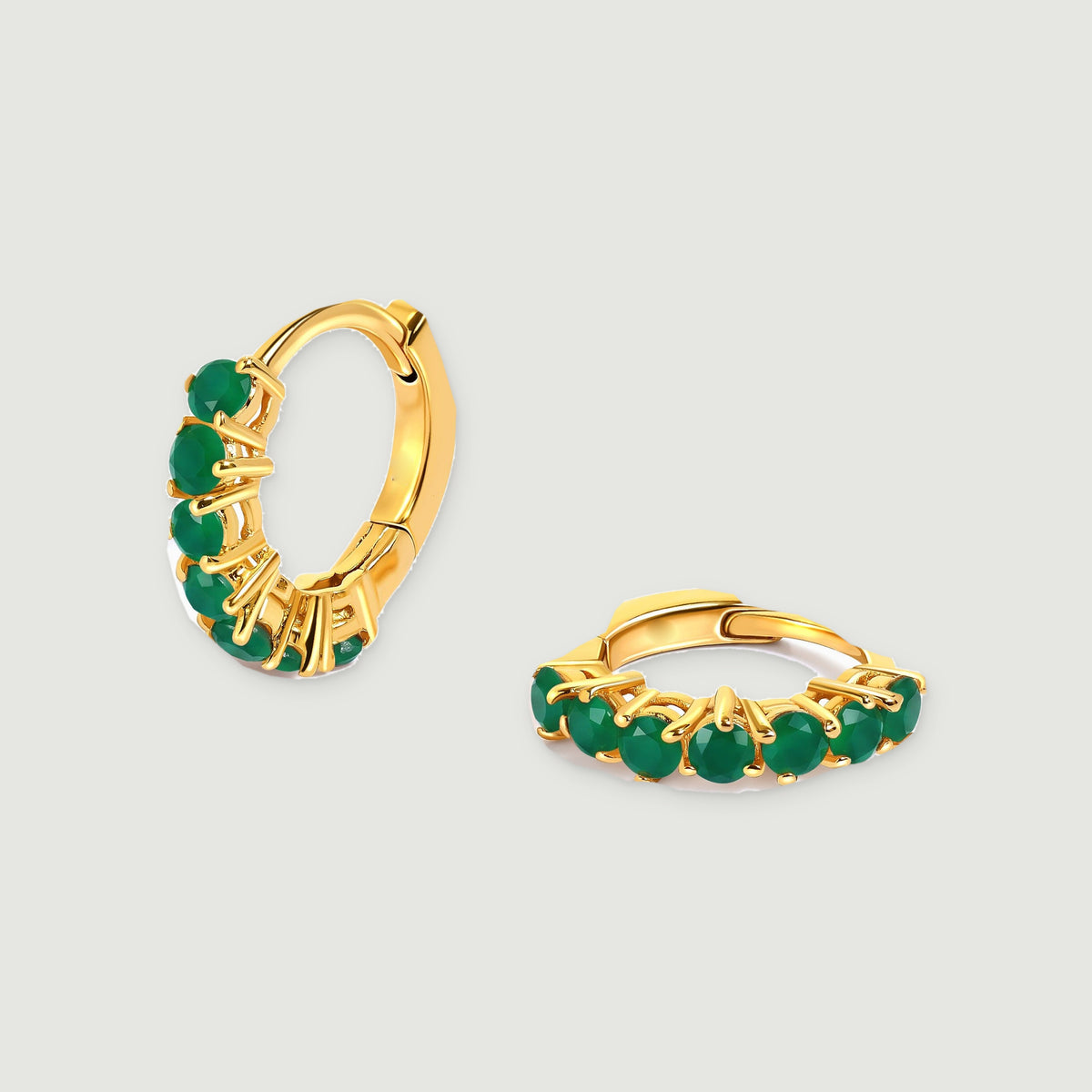 Two yellow gold plated hoop earrings with round green stones rest on a light gray background.