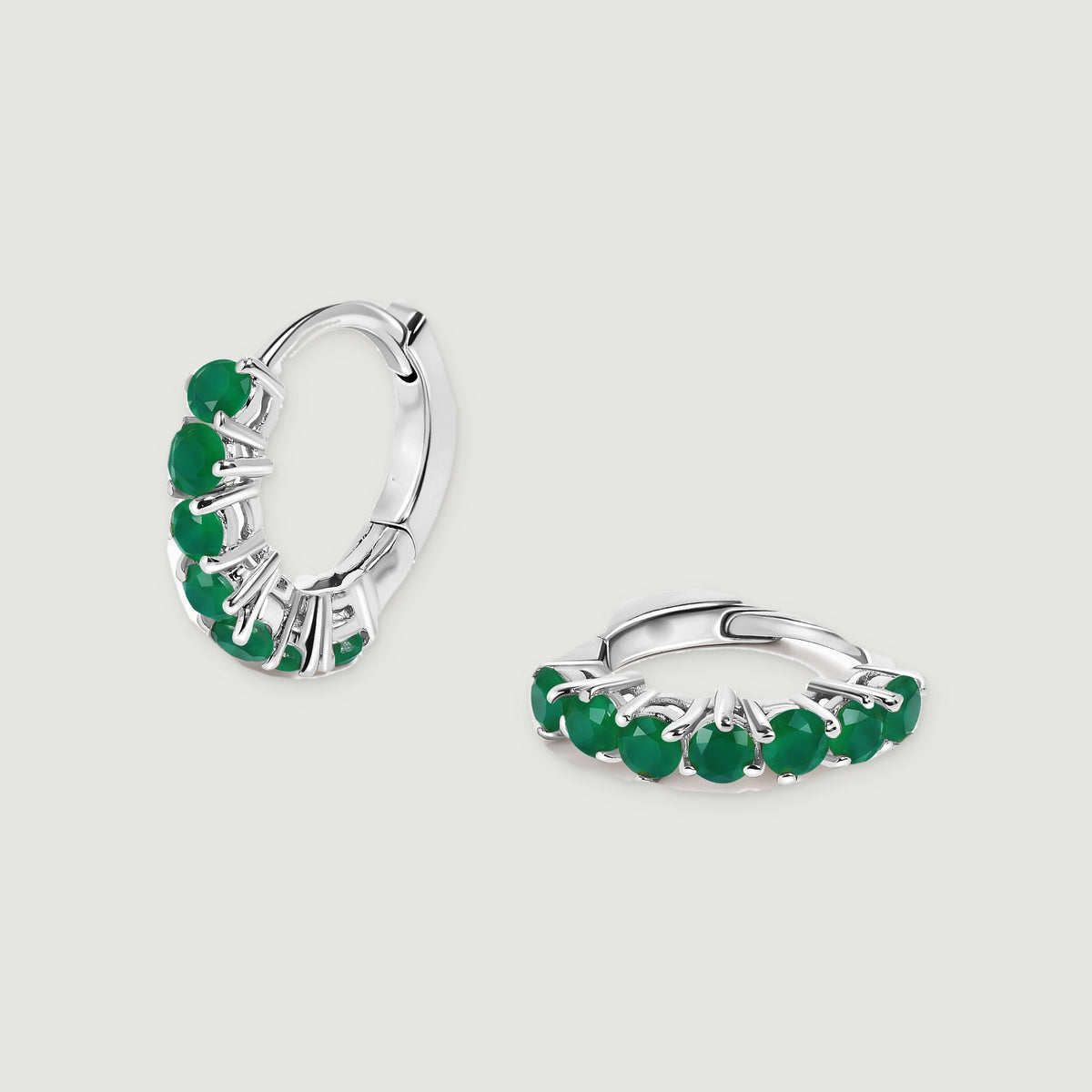 A pair of white rhodium plated hoops shows green gemstones and polished hinged closures on light gray.