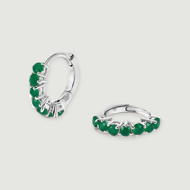A pair of white rhodium plated hoops shows green gemstones and polished hinged closures on light gray.