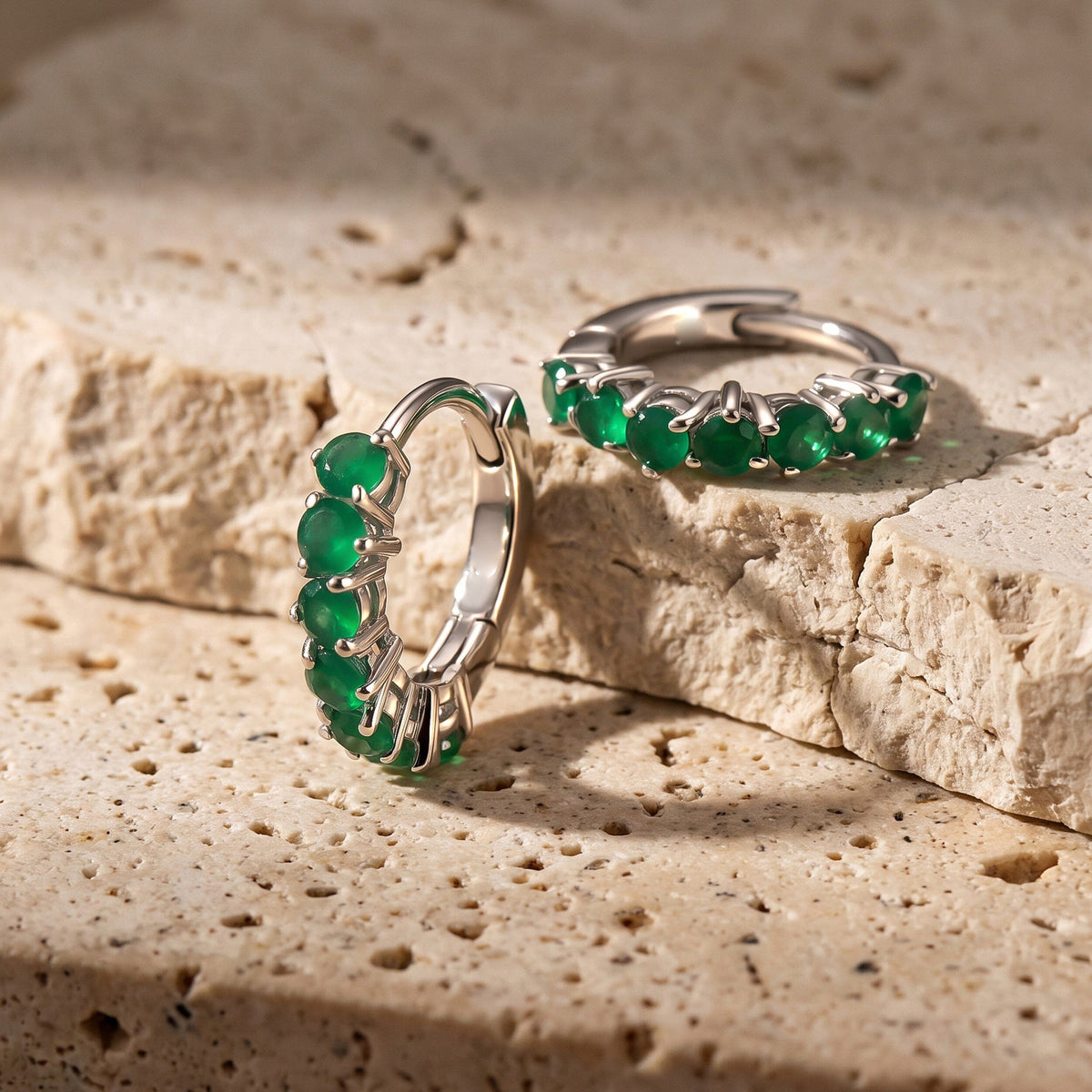 White rhodium plated earrings with green stones are arranged across a warm stone ledge.