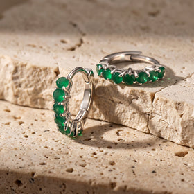 White rhodium plated earrings with green stones are arranged across a warm stone ledge.