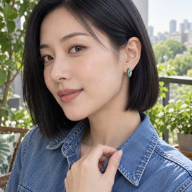 A woman with a black bob wears a white rhodium plated green onyx hoop on a leafy balcony.