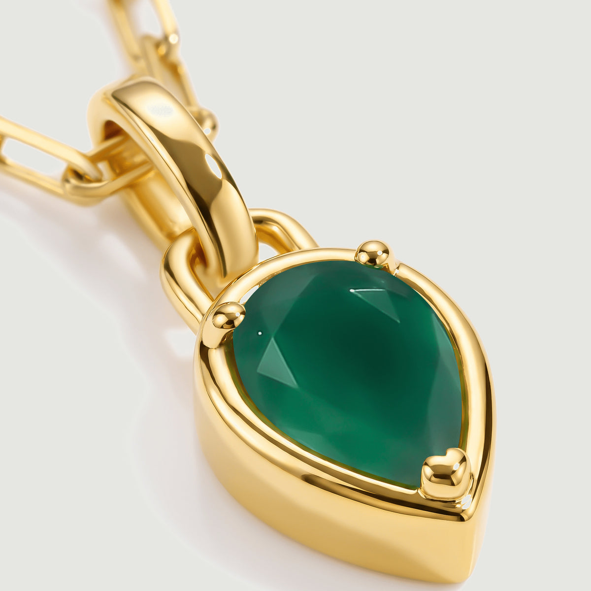 A close view shows green gemstone facets, three rounded prongs and the polished yellow gold plated pendant rim.