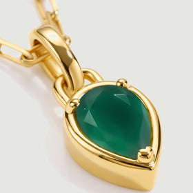 A close view shows green gemstone facets, three rounded prongs and the polished yellow gold plated pendant rim.