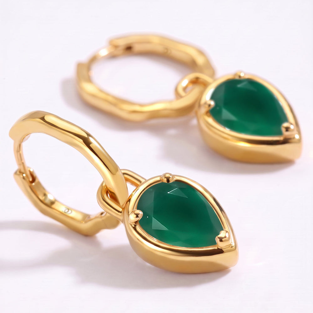 A close view shows the green stone facets, three prongs and polished gold edges of the earrings.