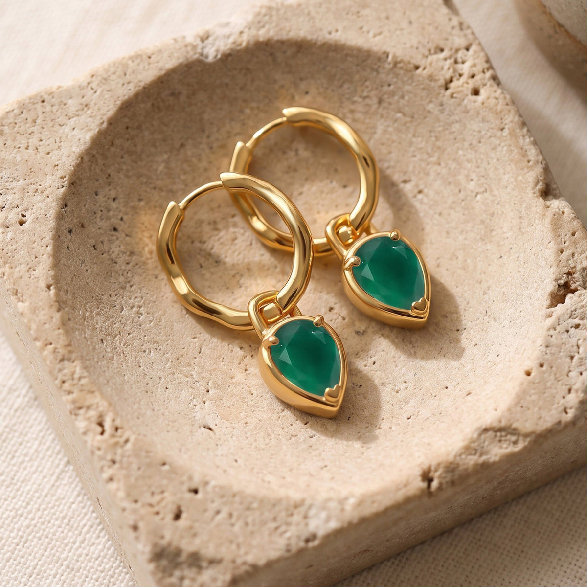Yellow gold plated earrings lie together on a textured beige stone tray.