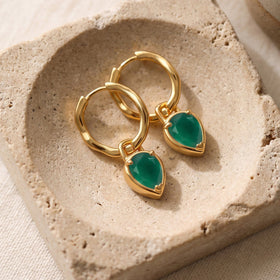 Yellow gold plated earrings lie together on a textured beige stone tray.