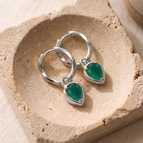 White rhodium plated hoops with green drops are arranged diagonally on a beige stone tray.