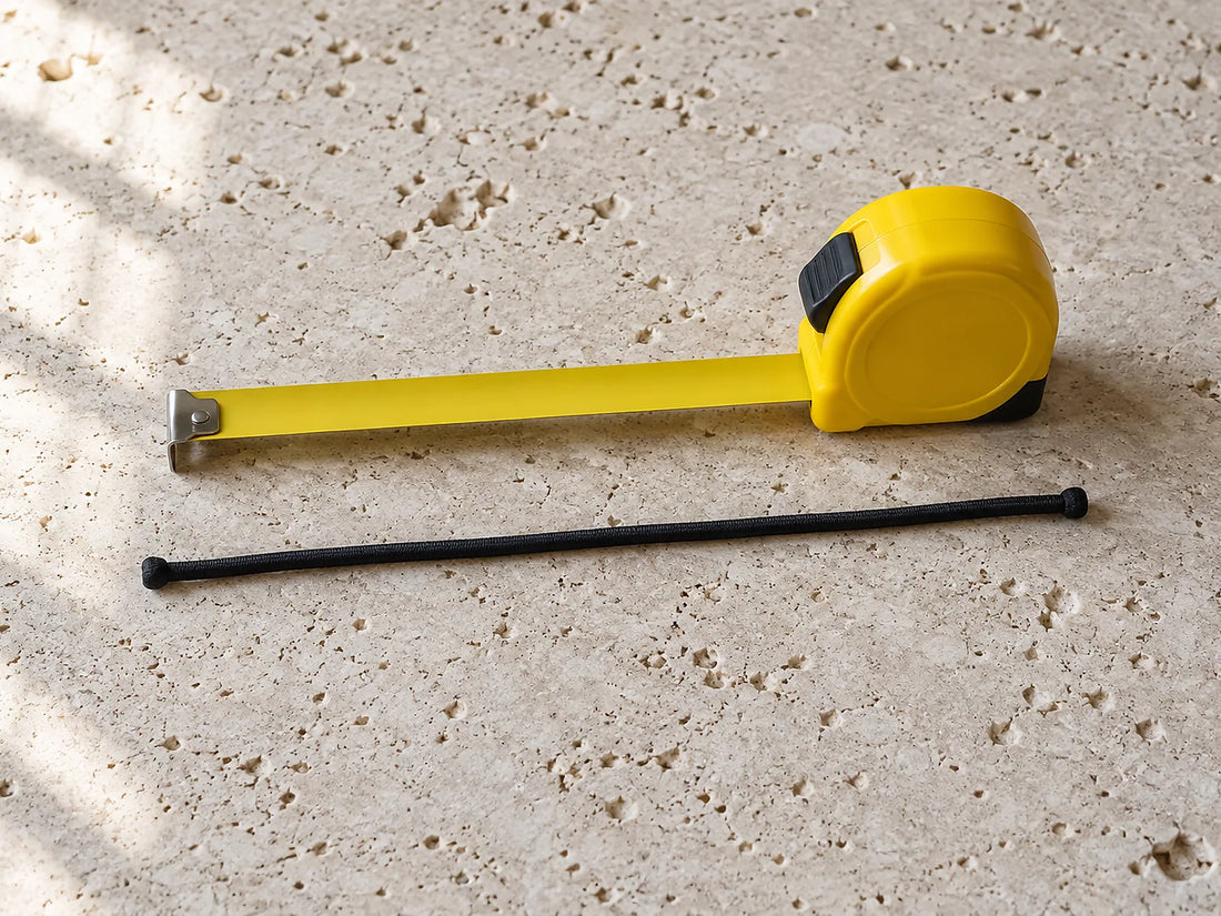 Natural window light illuminates one straight unjoined elastic cord alongside an unmarked measuring tape.