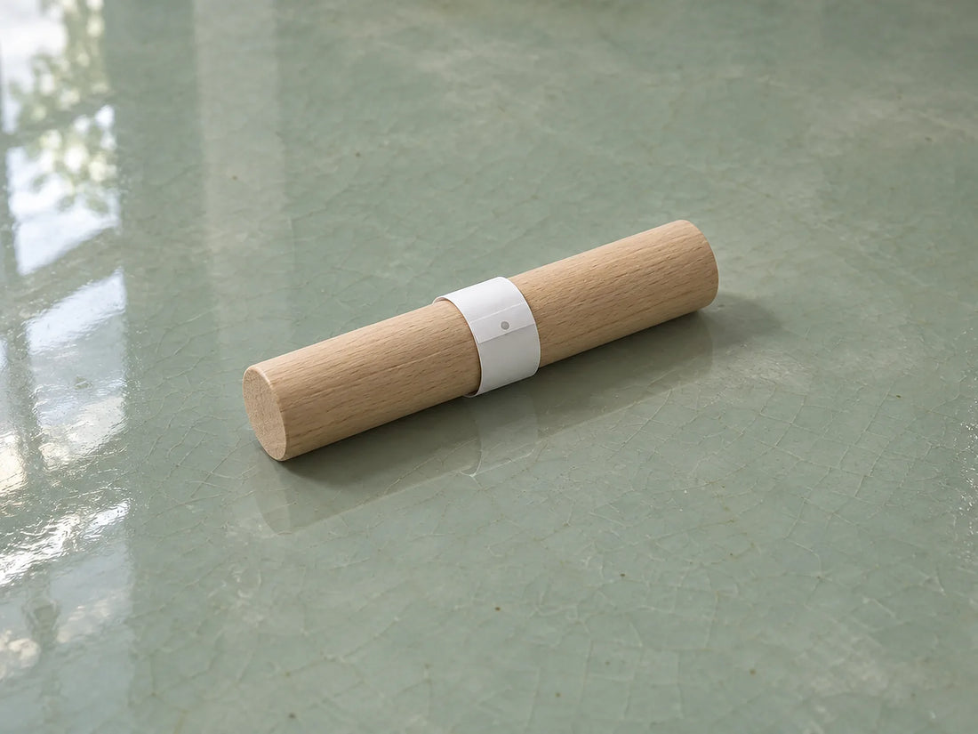 Natural window light illuminates a narrow plain paper strip wrapped around an abstract smooth wooden dowel.
