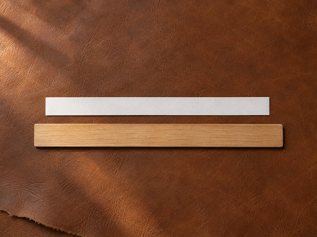 Natural window light illuminates a narrow paper sizing strip laid flat beside an unmarked ruler.