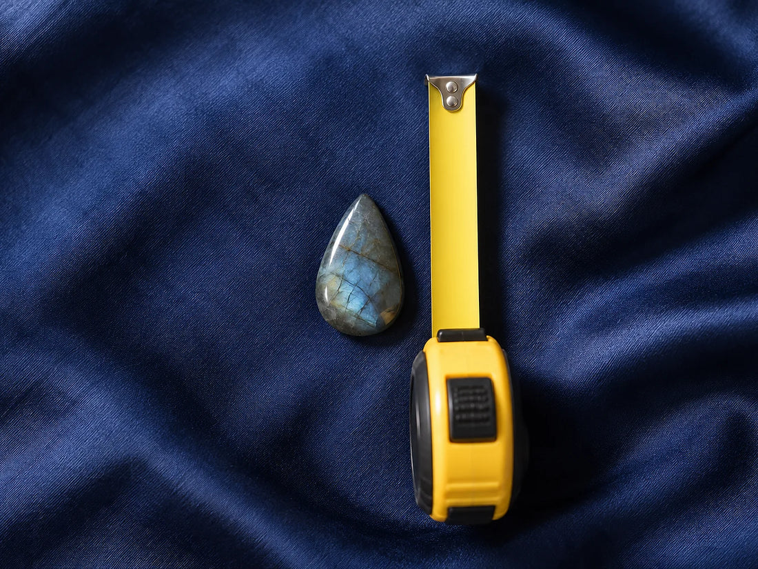 Natural window light illuminates one small unmounted teardrop stone beside an unmarked measuring tape.