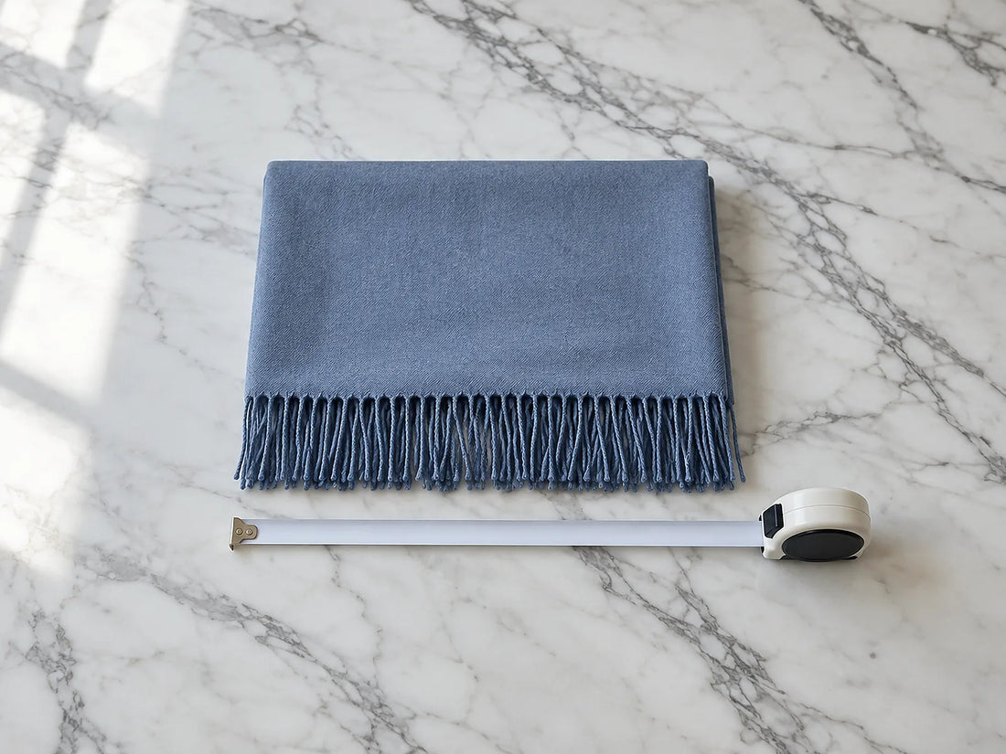 Natural window light illuminates one folded scarf alongside a blank measuring tape showing its width.