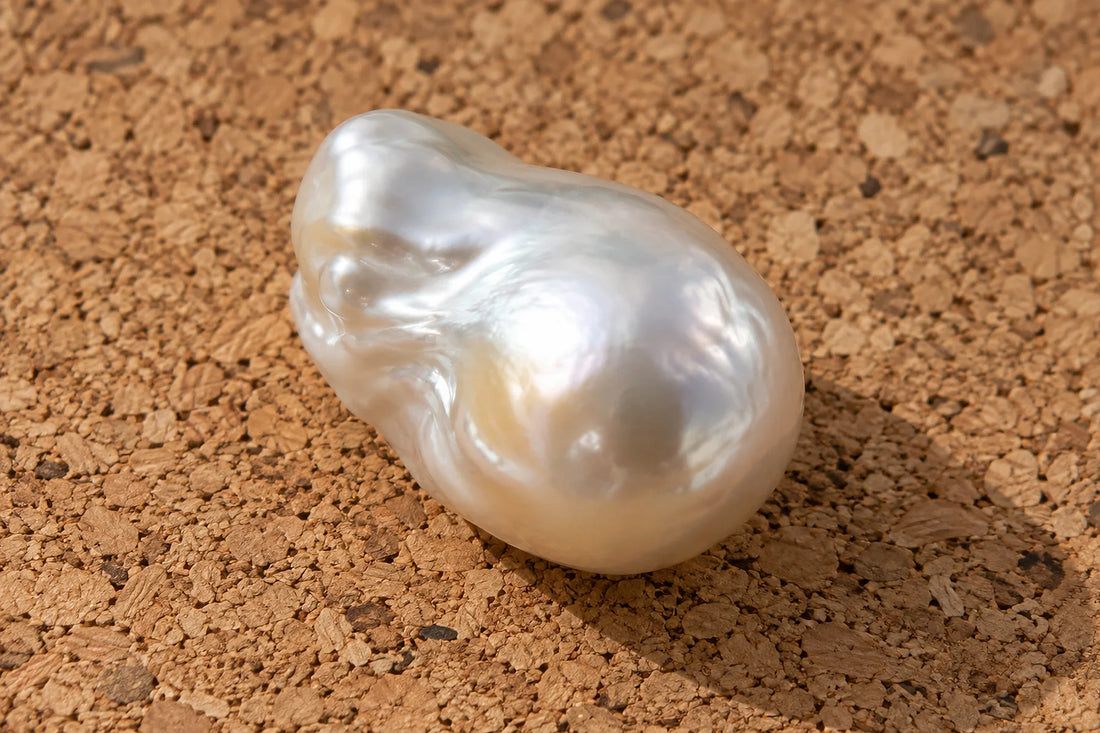 Natural window light illuminates one loose unmounted baroque pearl with luminous white nacre.
