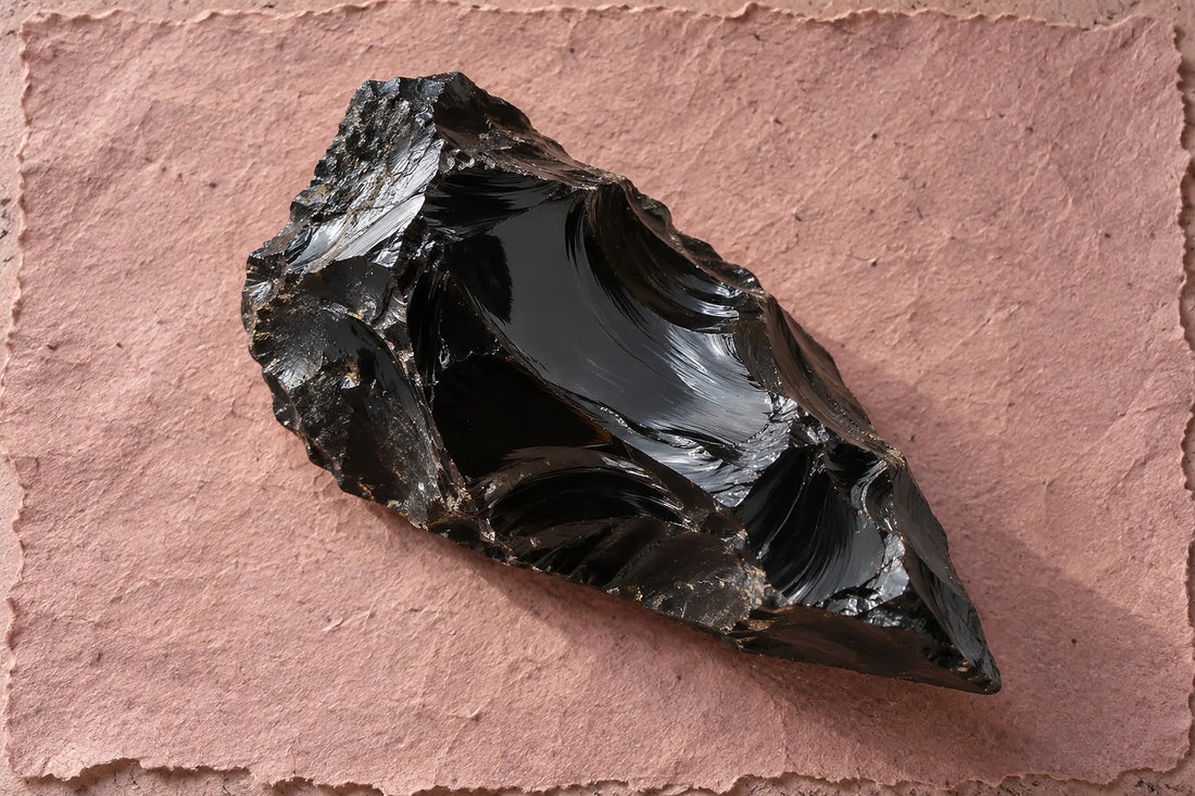 Natural window light illuminates one irregular glossy black obsidian fragment with sharp edges.