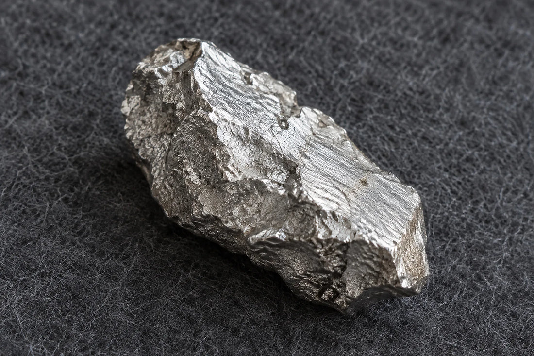 Natural window light illuminates one rough silver-metal fragment with a cool white metallic surface.