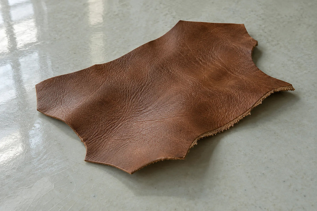 Natural window light illuminates one saddle-brown leather offcut with a raw fibrous cut edge.