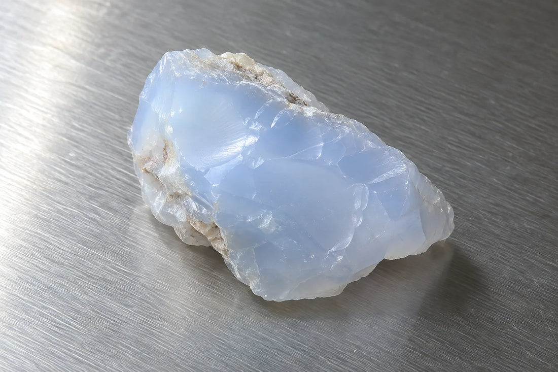 Natural window light illuminates one soft milky-blue chalcedony fragment with waxy translucence.