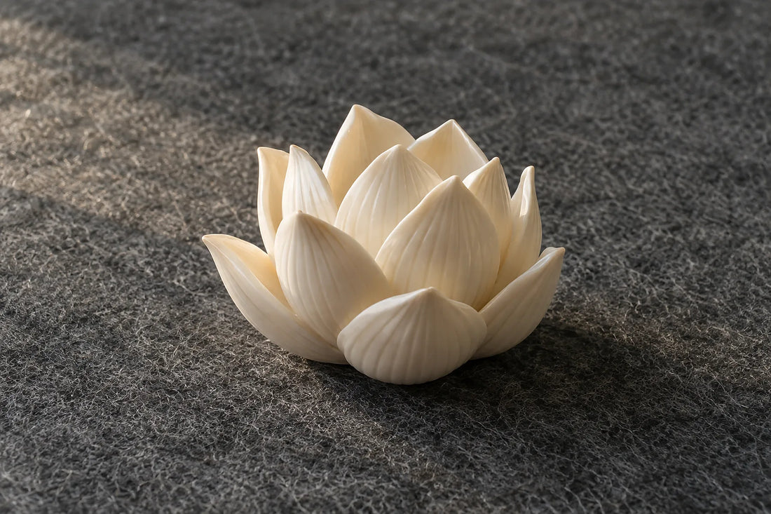Natural window light illuminates one small ivory ceramic lotus sculpture, complete layered petals.