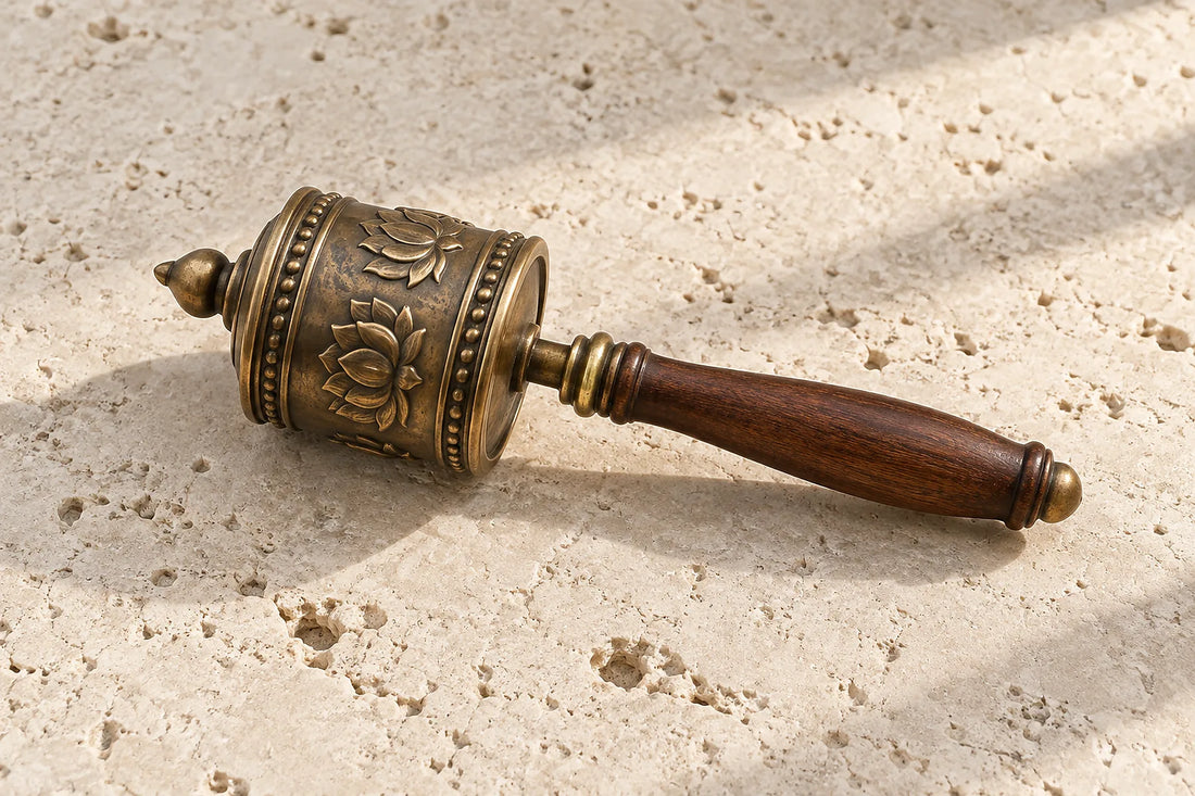Natural window light illuminates one complete bronze Buddhist prayer wheel with a clear turning axle and handle, pictorial lotus relief ONLY, no letters or scripture.
