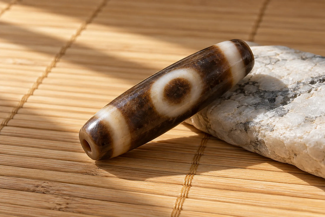 Natural window light illuminates one unstrung long cylindrical brown-and-ivory agate Dzi bead with ONE irregular eye motif.
