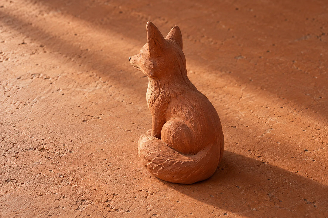 Natural window light illuminates one small terracotta fox sculpture with complete ears and a curled tail.