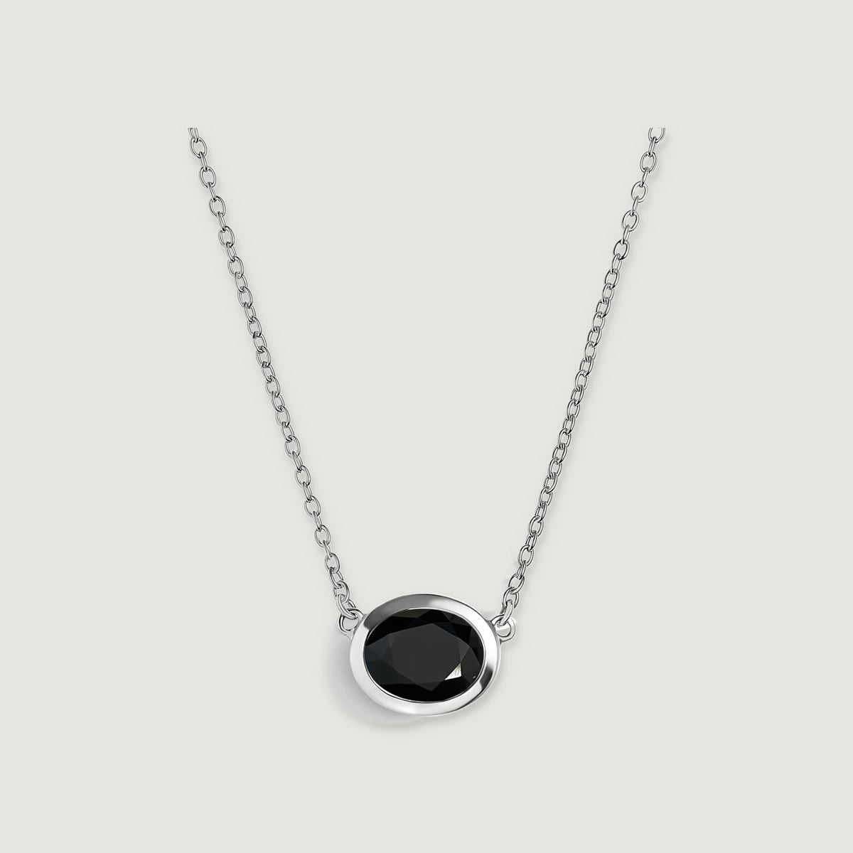 An oval black obsidian pendant sits in a polished white-rhodium-plated bezel on a matching chain.