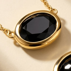 A close view shows the glossy facets of black obsidian framed by a smooth yellow-gold-plated bezel.