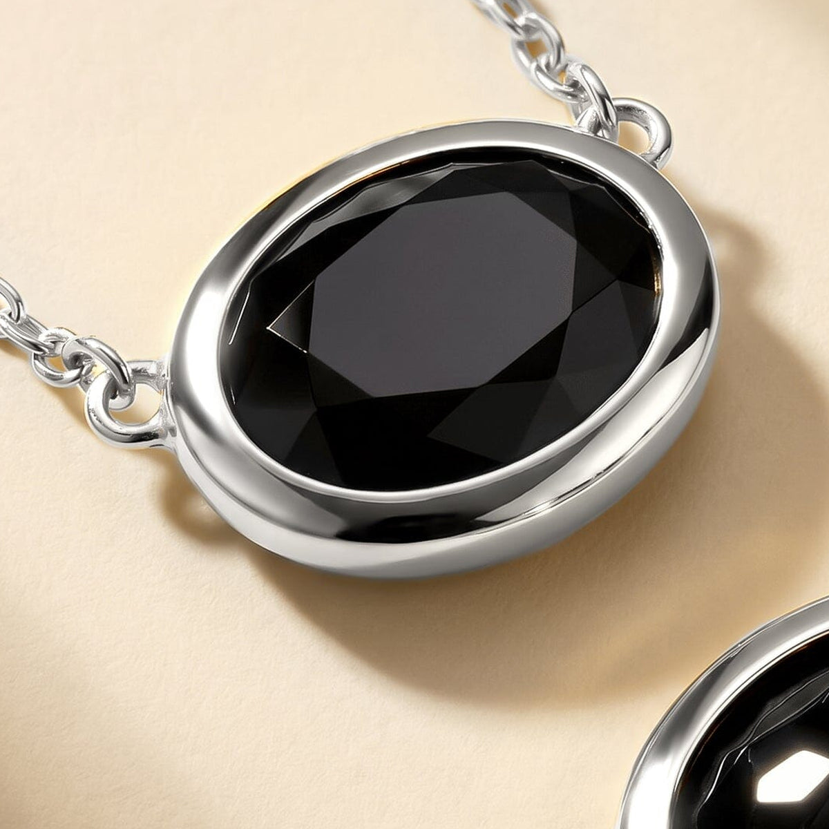 The white-rhodium-plated setting catches the light around a black oval pendant on a pale beige surface.