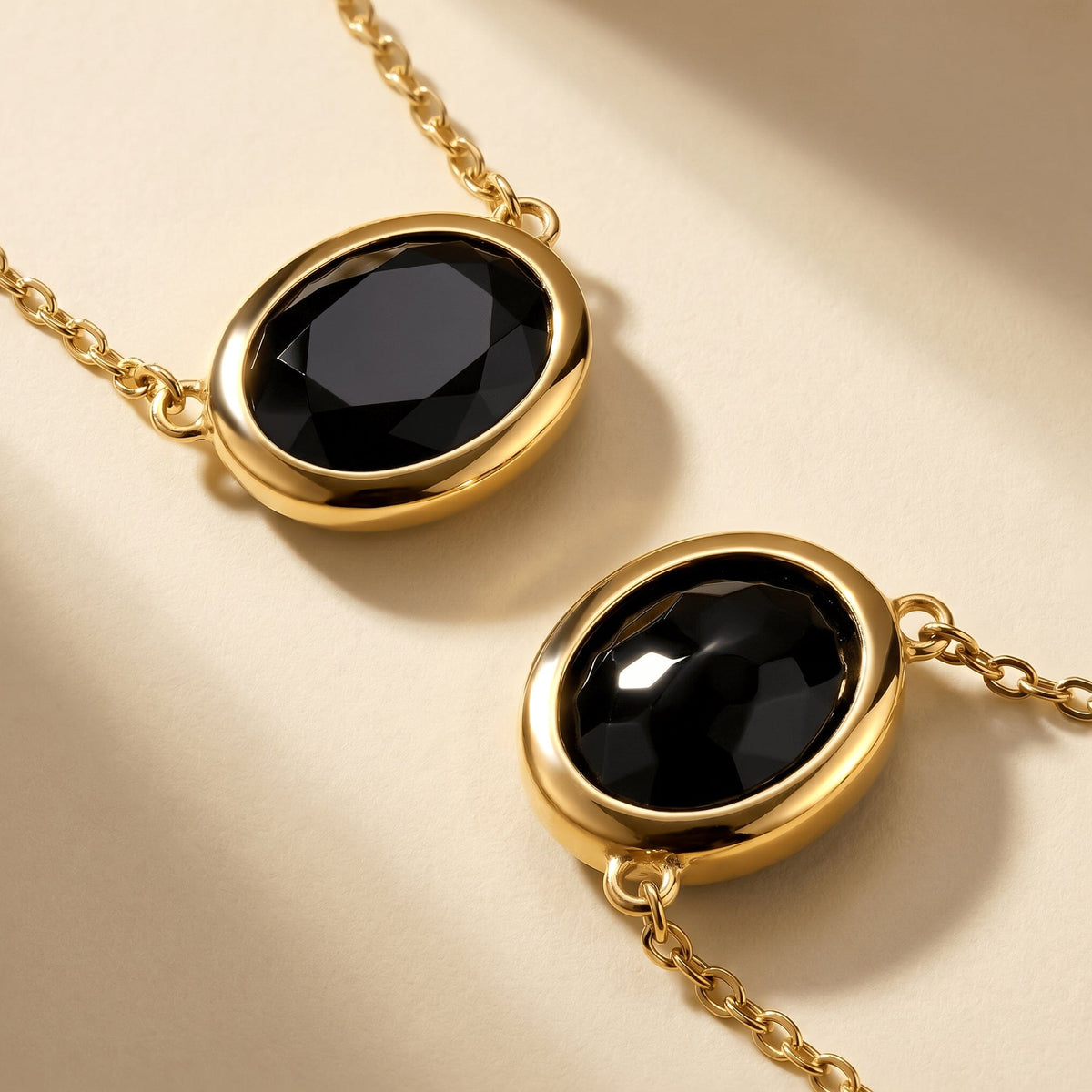 Two yellow-gold-plated black obsidian pendants lie diagonally on a clean pale beige surface.