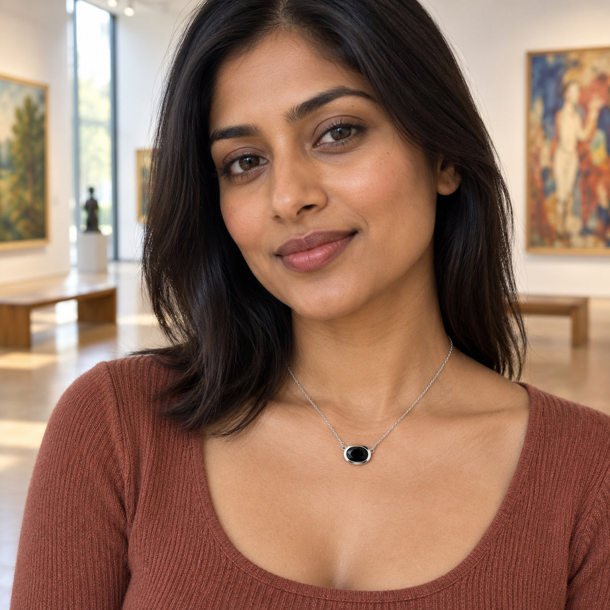 A woman in a rust-colored knit top wears a white-rhodium-plated black obsidian necklace in an art gallery.