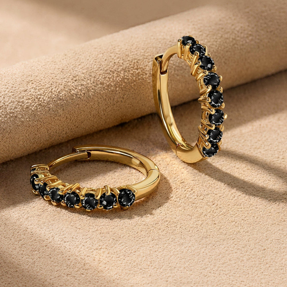 Yellow gold plated black stone hoops rest beside a folded beige suede surface.