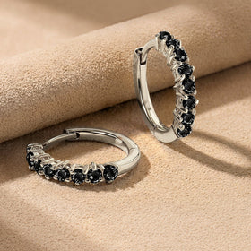 White rhodium plated hoop earrings lie on beige suede with their black stones facing forward.