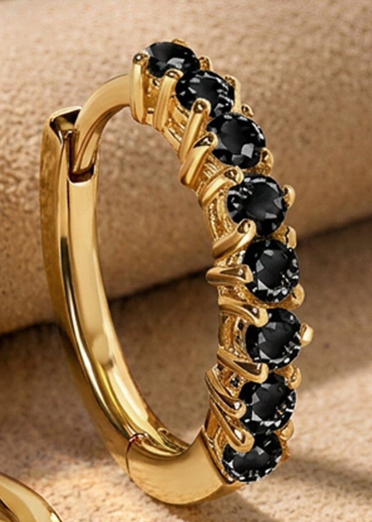 A close view shows faceted black stones held by yellow gold plated prongs on a small hoop.