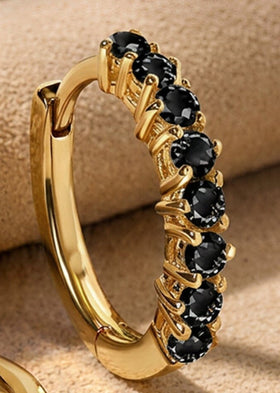 A close view shows faceted black stones held by yellow gold plated prongs on a small hoop.