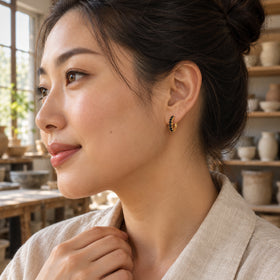 A woman with dark hair in a bun wears a yellow gold plated black stone hoop beside shelves of pottery.