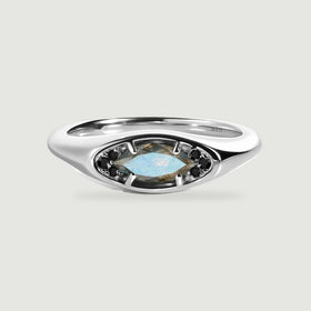 A polished silver ring with a blue-gray marquise labradorite and dark accent stones rests on a light gray surface.
