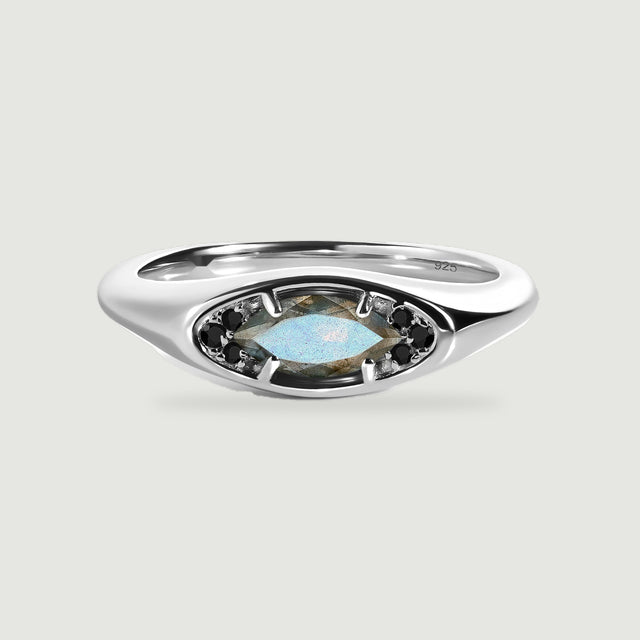A polished silver ring with a blue-gray marquise labradorite and dark accent stones rests on a light gray surface.