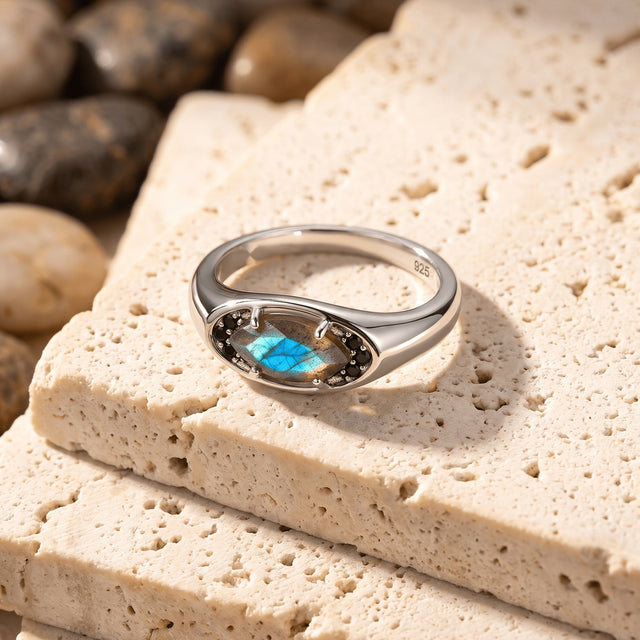 The silver ring rests at an angle on cream-colored stone with its blue labradorite facing forward.