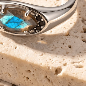 The curved silver shoulder and raised labradorite setting appear in an angled view against a pale stone surface.