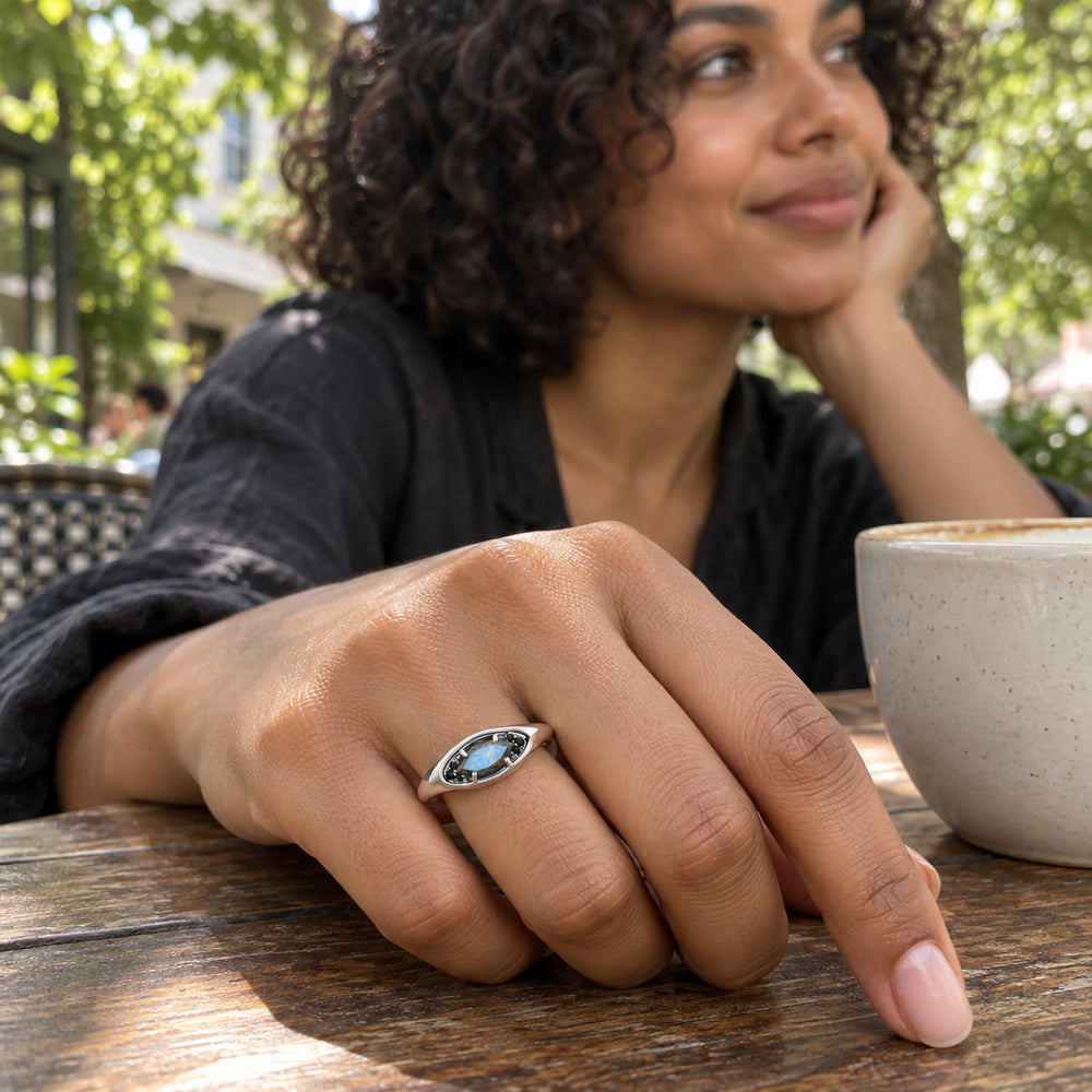 A woman with curly dark hair wears the silver labradorite ring while resting her hand beside a ceramic cup at an outdoor cafe.