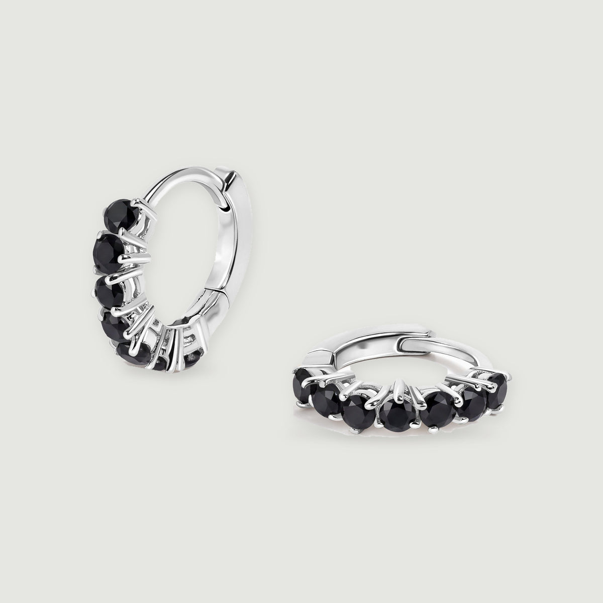 A pair of white rhodium plated earrings shows round black stones and hinged hoops.