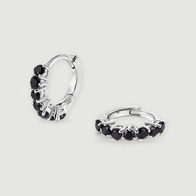 A pair of white rhodium plated earrings shows round black stones and hinged hoops.